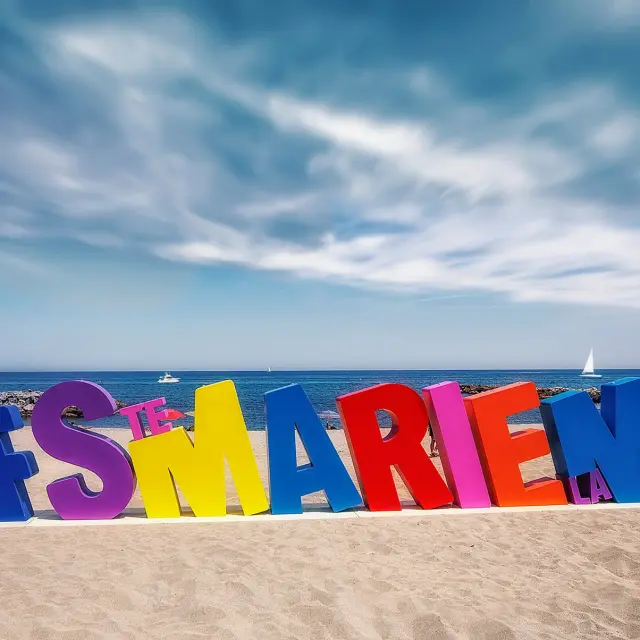 Installation colorée en forme de lettres géantes formant le mot « #STEMARIELAMER » sur la plage de Sainte-Marie-la-Mer, face à la Méditerranée.