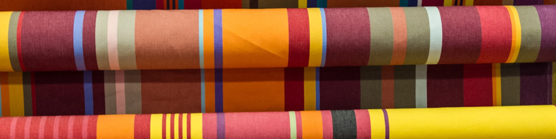 Rouleaux de tissus catalans aux rayures colorées, déclinant des tons chauds de rouge, jaune, orange et vert.