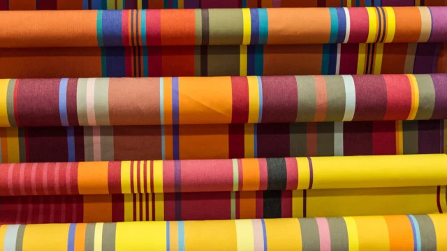 Rouleaux de tissus catalans aux rayures colorées, déclinant des tons chauds de rouge, jaune, orange et vert.
