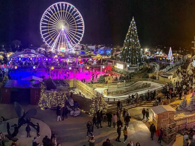Village de Noël du Barcarès de nuit avec grande roue illuminée, patinoire, sapin géant décoré et foule de visiteurs profitant des animations.
