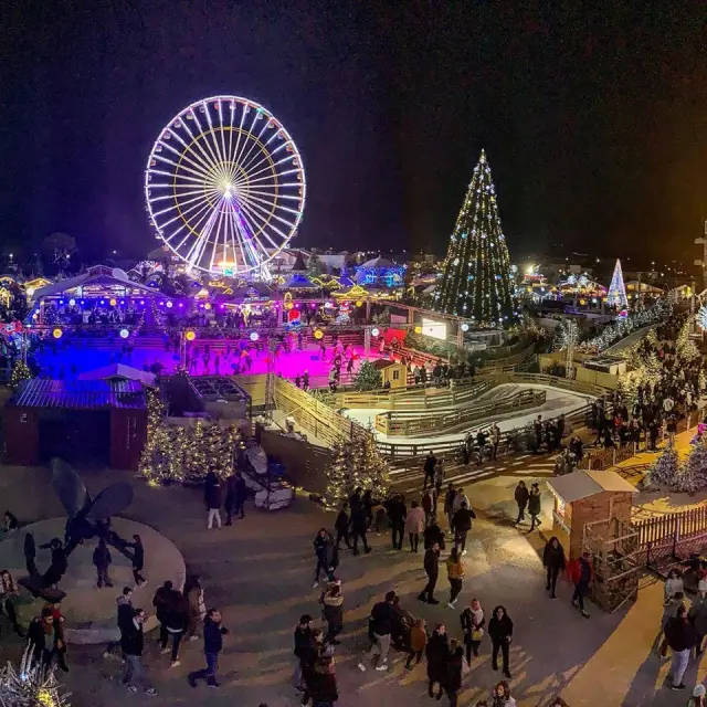 Village de Noël du Barcarès de nuit avec grande roue illuminée, patinoire, sapin géant décoré et foule de visiteurs profitant des animations.