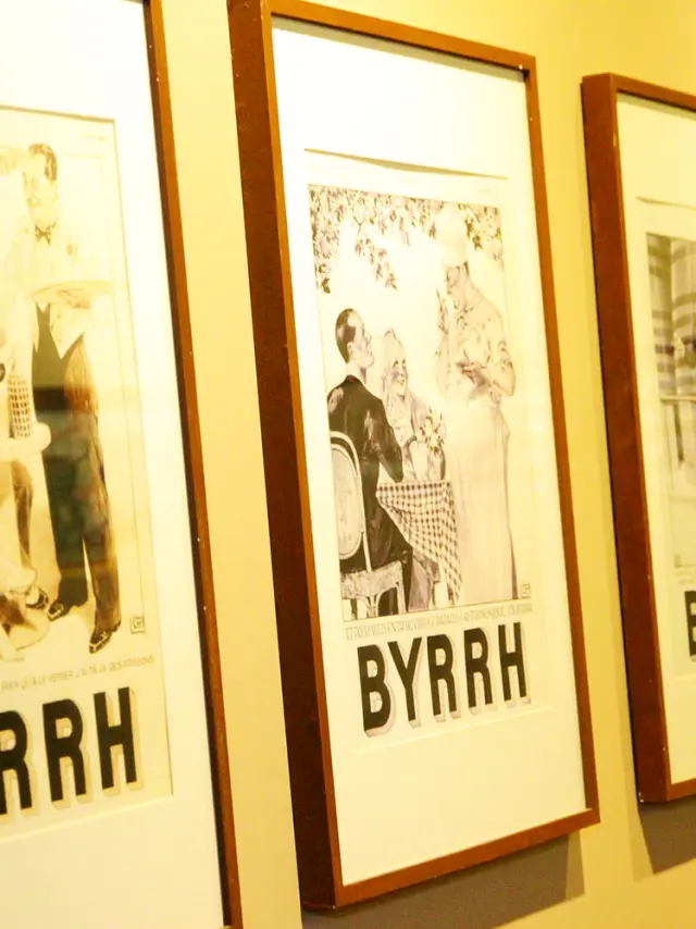 Série d’affiches publicitaires anciennes en noir et blanc de la marque Byrrh, encadrées et exposées sur un mur à la Cave Byrrh de Thuir, illustrant l’évolution du style graphique et de la communication de la marque au fil du temps.