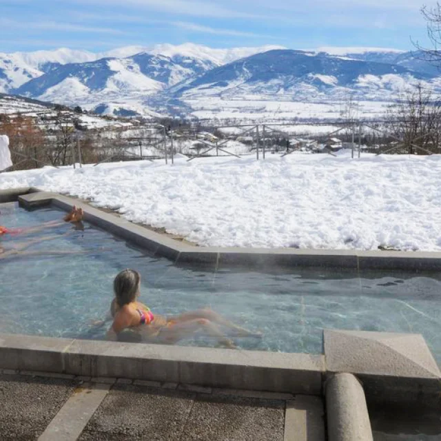 Personnes se relaxant dans un bassin extérieur des Bains de Dorres entouré de neige, avec vue sur les montagnes enneigées de Cerdagne.