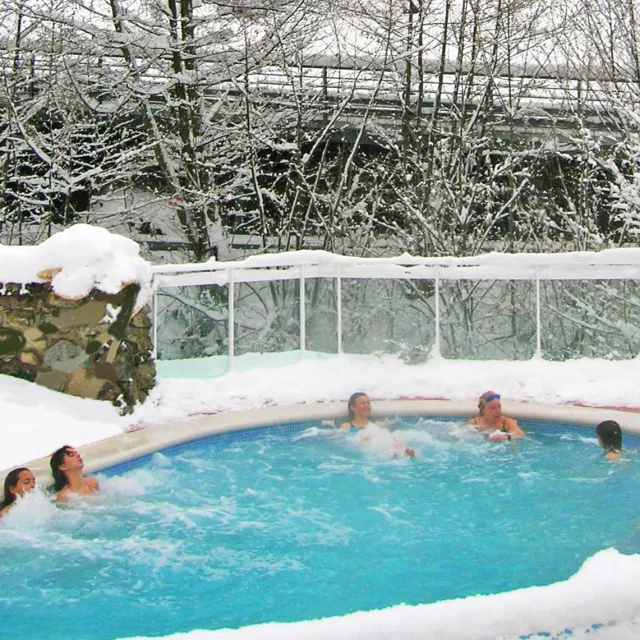Personnes se baignant dans un bassin extérieur des Bains de Llo entouré de neige, avec des arbres enneigés en arrière-plan.