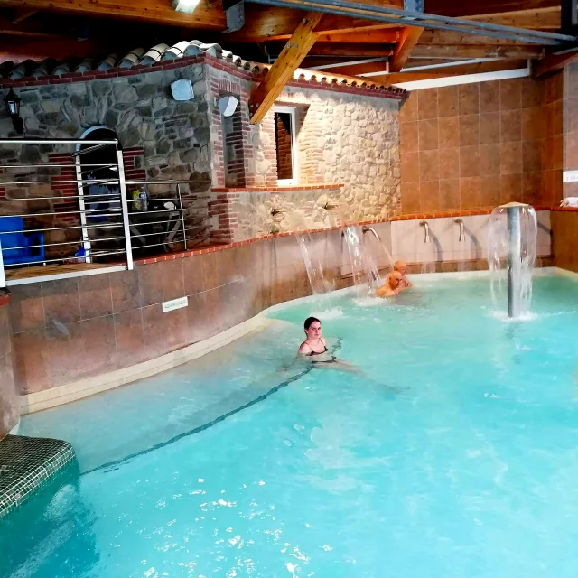 Bassin intérieur des Bains de Saint-Thomas avec cascades d’eau thermale et espace de détente sous une charpente en bois.