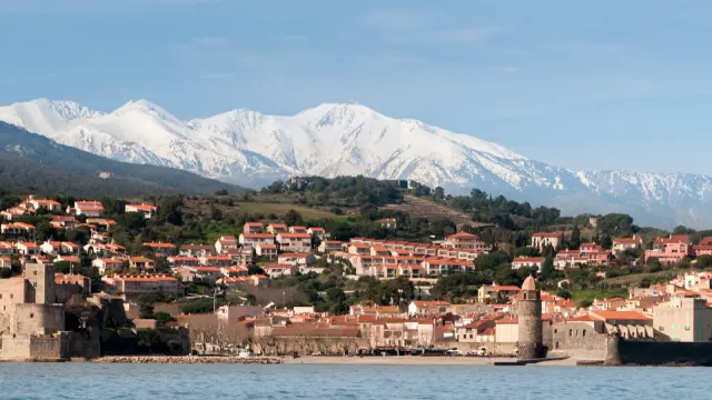 Vue sur Collioure et son clocher emblématique, avec les toits aux tuiles rouges du village et le massif du Canigó enneigé en arrière-plan.