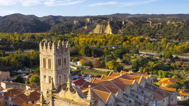 Vue aérienne de l’église Saint-Étienne d’Ille-sur-Têt avec les toits du village et les Orgues en arrière-plan.