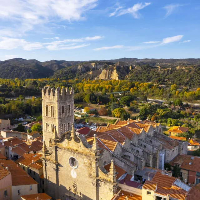 Vue aérienne de l’église Saint-Étienne d’Ille-sur-Têt avec les toits du village et les Orgues en arrière-plan.