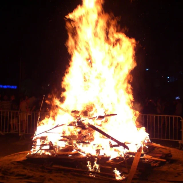Grand feu de la Saint-Jean s’élevant dans la nuit, entouré de spectateurs derrière des barrières, lors des célébrations de la Sant Joan en Catalogne Nord.