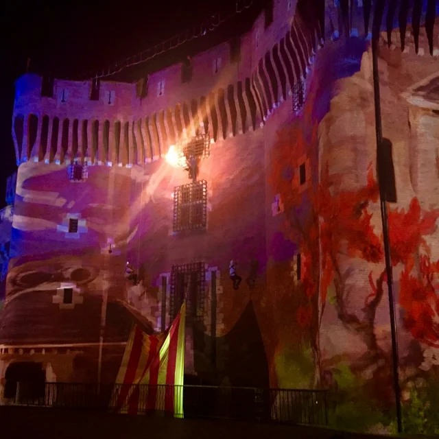 Projection lumineuse sur la façade du Castillet à Perpignan, monument emblématique de la ville, éclairé de couleurs vives et d’animations nocturnes célébrant la culture catalane.