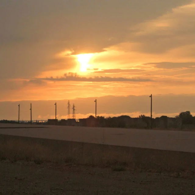 Lever du soleil sur le Mémorial du Camp de Rivesaltes, illuminant le ciel de teintes dorées et orangées au-dessus du site historique.