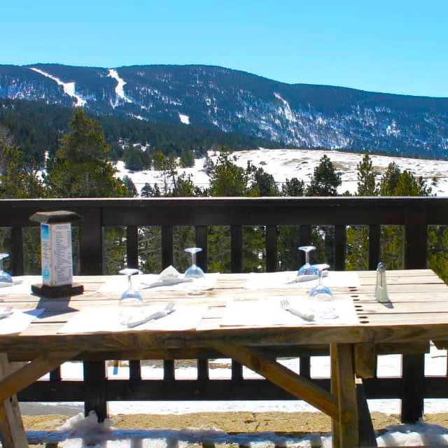 Table en bois dressée en terrasse du refuge des Bouillouses, avec vue panoramique sur les montagnes enneigées et les pistes de ski du Capcir.