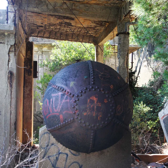 Vestige industriel du site de Paulilles : une ancienne sphère métallique rivetée, installée dans les ruines en béton armé d’un ancien bâtiment des dynamiteries Alfred Nobel. L’ensemble est partiellement recouvert de graffitis, entouré de végétation et baigné de lumière naturelle.