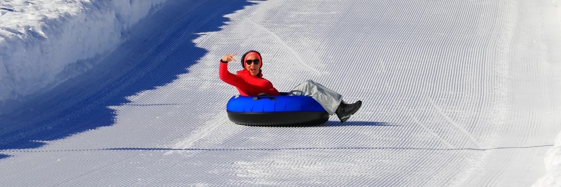 Personne descendant seule une piste enneigée sur une bouée bleue de snowtubing.