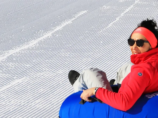 Personne descendant une piste de neige assise sur une bouée bleue de snowtubing.