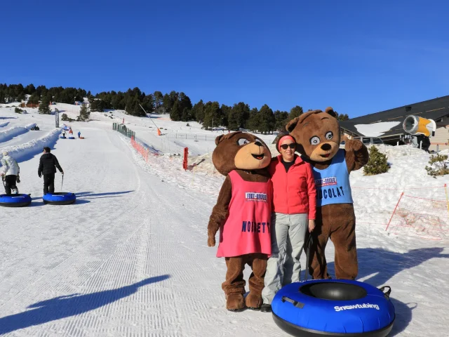 Personne posant avec les mascottes Noisette et Chocolat sur la piste de snowtubing de Font-Romeu, sous un ciel bleu.