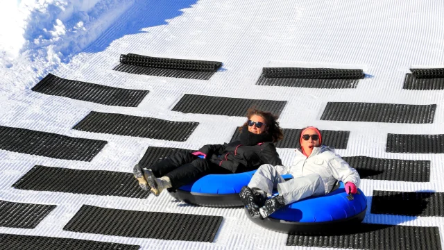 Deux personnes glissant sur des bouées bleues de snowtubing sur une piste enneigée.