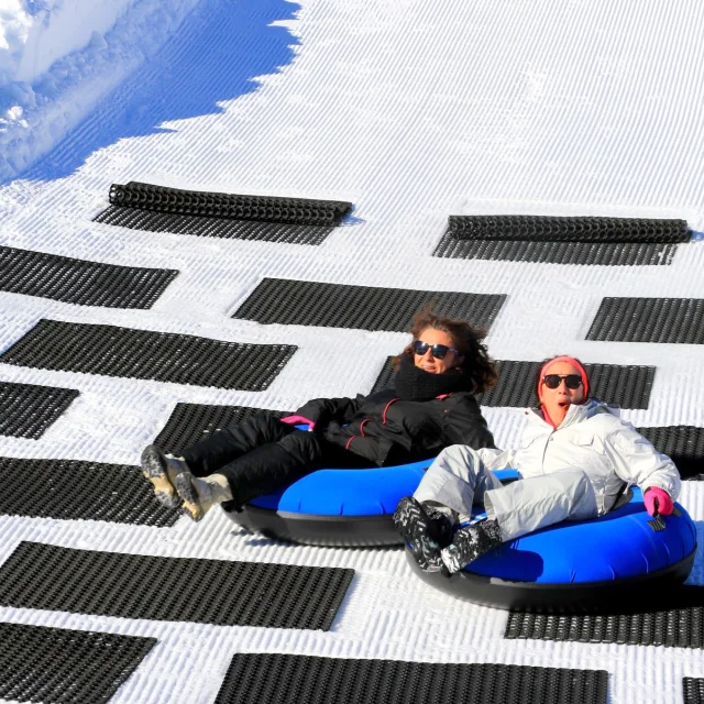 Deux personnes glissant sur des bouées bleues de snowtubing sur une piste enneigée.