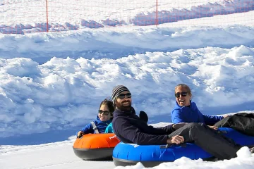 Trois personnes glissant sur des bouées de snowtubing sur une piste enneigée.