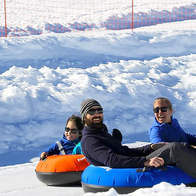 Trois personnes glissant sur des bouées de snowtubing sur une piste enneigée.