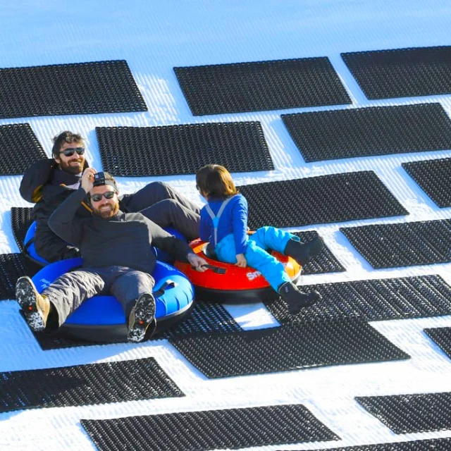 Trois personnes glissant sur des bouées de snowtubing sur une piste enneigée.