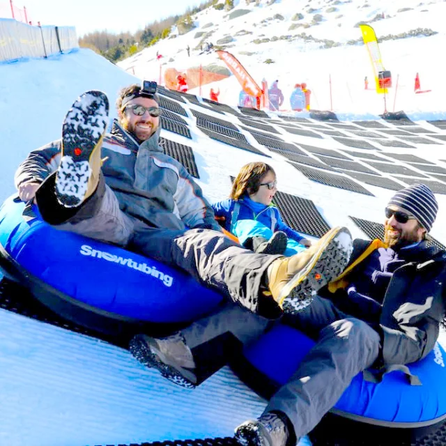Trois personnes descendant une piste enneigée sur des bouées bleues de snowtubing.