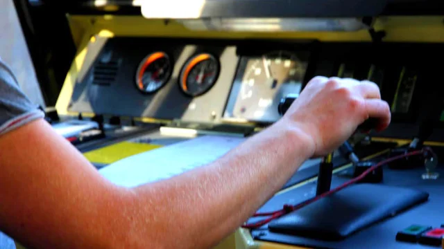 Gros plan sur le poste de conduite du Train Jaune, montrant le bras du conducteur manipulant les commandes et les leviers de contrôle à bord de la cabine.