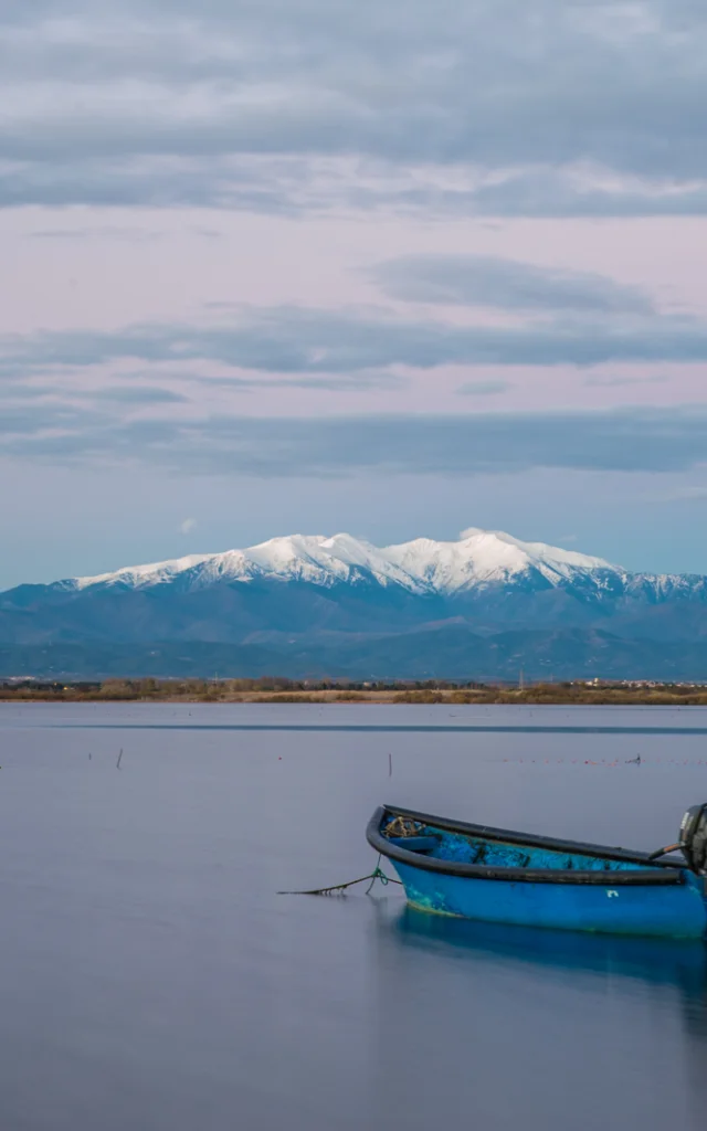 Deux barques bleues sur l’étang de Canet-Saint-Nazaire avec le Canigó enneigé en arrière-plan.
