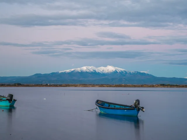 Deux barques bleues sur l’étang de Canet-Saint-Nazaire avec le Canigó enneigé en arrière-plan.