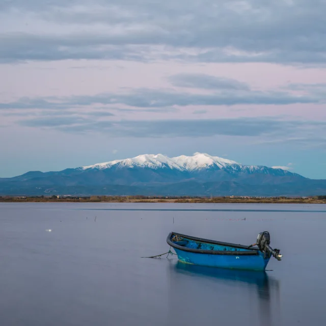Deux barques bleues sur l’étang de Canet-Saint-Nazaire avec le Canigó enneigé en arrière-plan.
