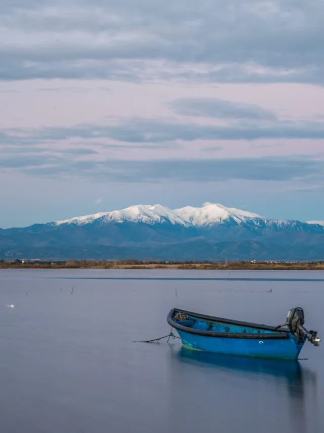 Deux barques bleues sur l’étang de Canet-Saint-Nazaire avec le Canigó enneigé en arrière-plan.