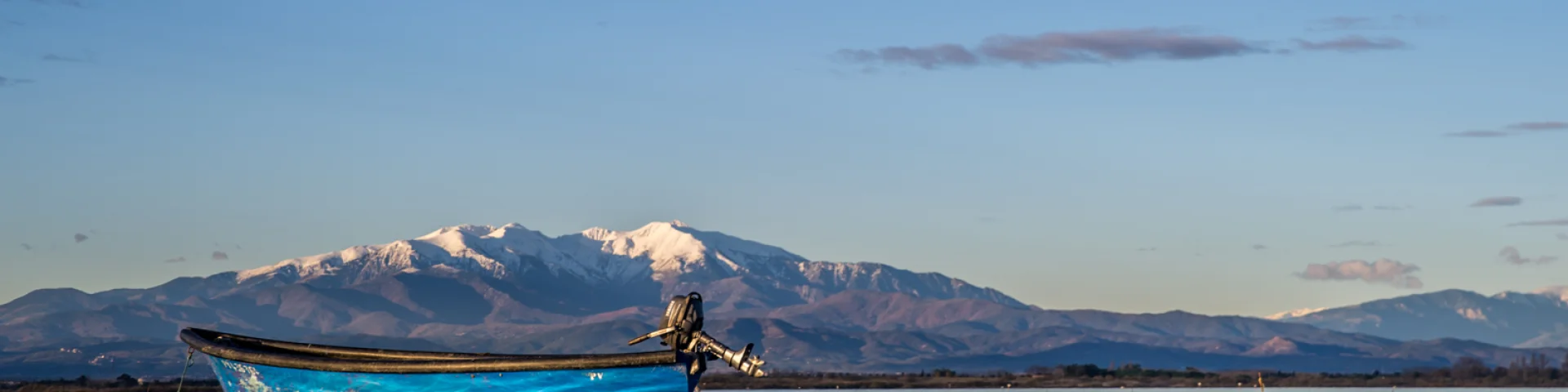 Barque bleue sur l’étang de Canet-Saint-Nazaire avec le Canigó enneigé à l’horizon.