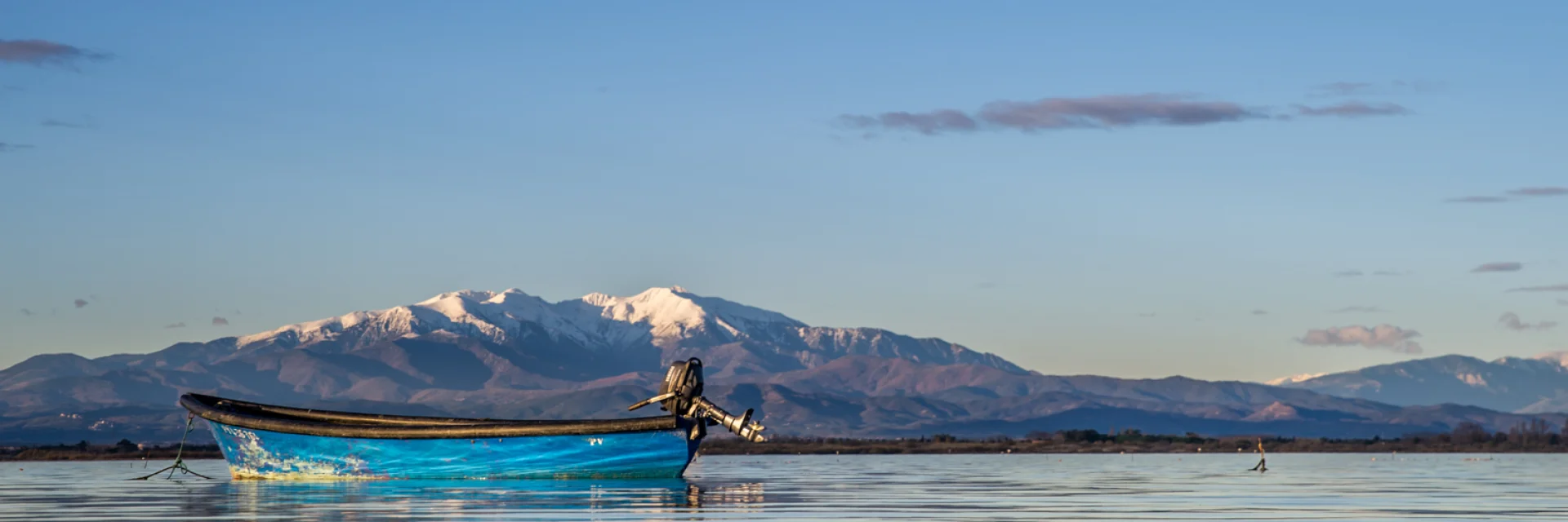 Barque bleue sur l’étang de Canet-Saint-Nazaire avec le Canigó enneigé à l’horizon.