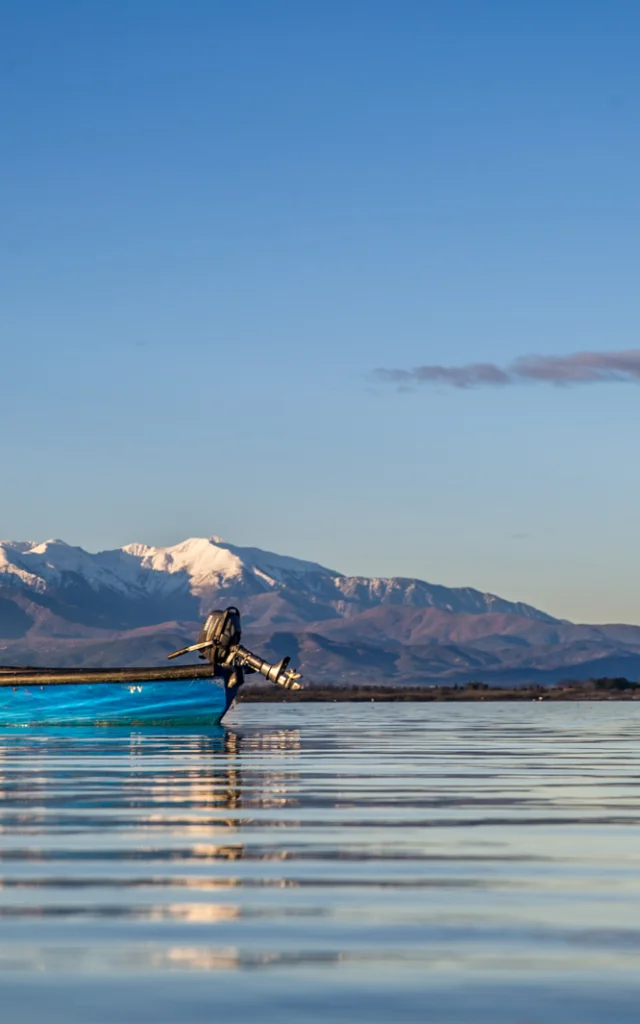 Barque bleue sur l’étang de Canet-Saint-Nazaire avec le Canigó enneigé à l’horizon.