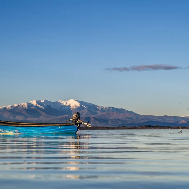 Barque bleue sur l’étang de Canet-Saint-Nazaire avec le Canigó enneigé à l’horizon.