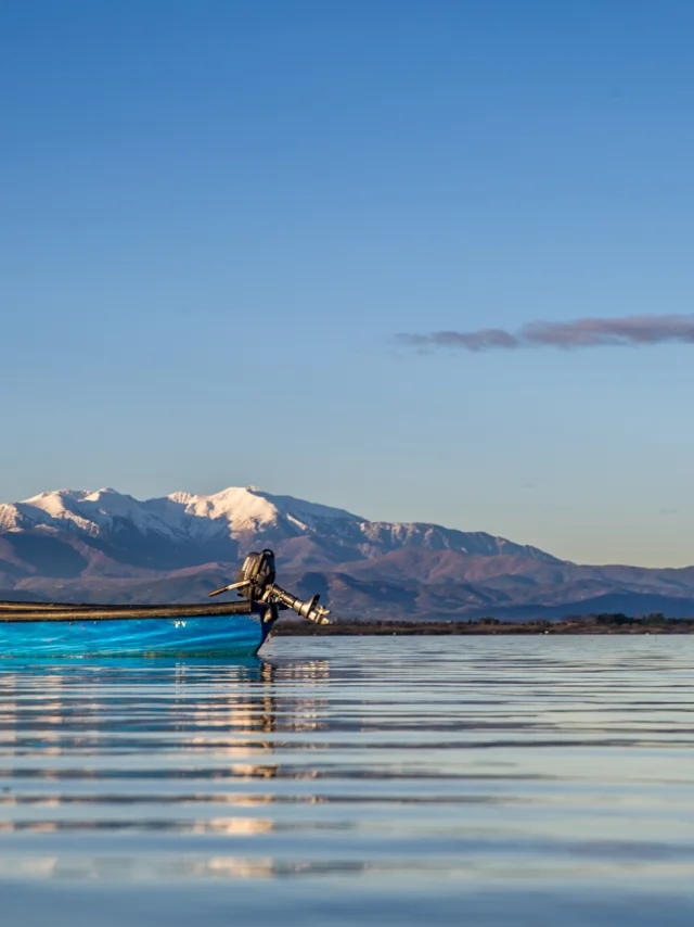 Barque bleue sur l’étang de Canet-Saint-Nazaire avec le Canigó enneigé à l’horizon.