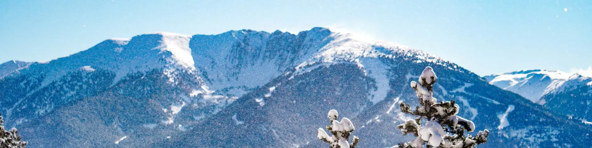 Vue sur les sommets enneigés du Cambre d’Aze avec des forêts de pins au premier plan sous un ciel bleu lumineux.
