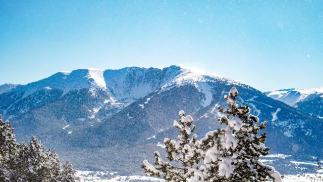Vue sur les sommets enneigés du Cambre d’Aze avec des forêts de pins au premier plan sous un ciel bleu lumineux.