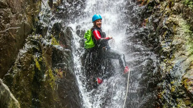 Personne descendant en rappel sous une cascade lors d’une sortie de canyoning à Thuès-les-Bains.