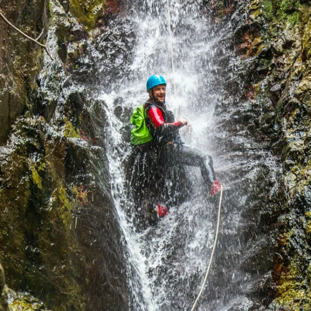 Personne descendant en rappel sous une cascade lors d’une sortie de canyoning à Thuès-les-Bains.