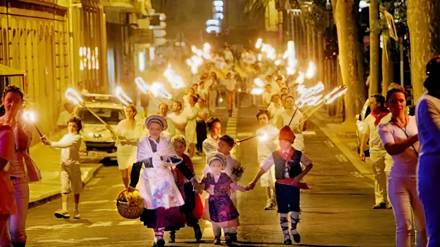 Défilé nocturne de la Sant Joan à Perpignan, avec des habitants vêtus de blanc portant des torches et des enfants en costumes traditionnels catalans en tête de cortège.