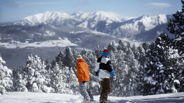 Deux snowboardeurs sur la piste de la Calme à Font-Romeu, avec une vue panoramique sur les montagnes enneigées des Pyrénées.