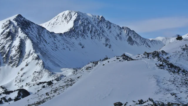 Vue sur un massif montagneux enneigé avec des sommets escarpés et des pentes couvertes de neige sous un ciel bleu clair.