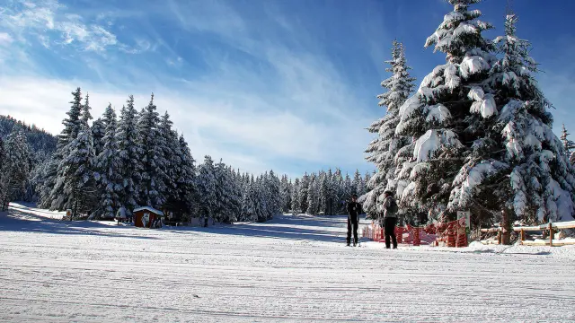 Paysage enneigé de la Station Nordique du Capcir avec des skieurs et des sapins couverts de neige sous un ciel bleu.