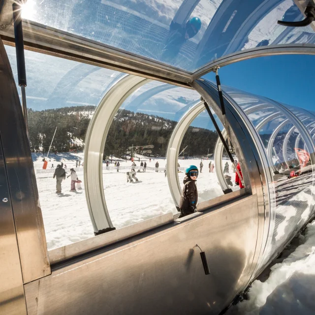 Enfant utilisant un tapis roulant couvert sur une piste de ski à Formiguères.
