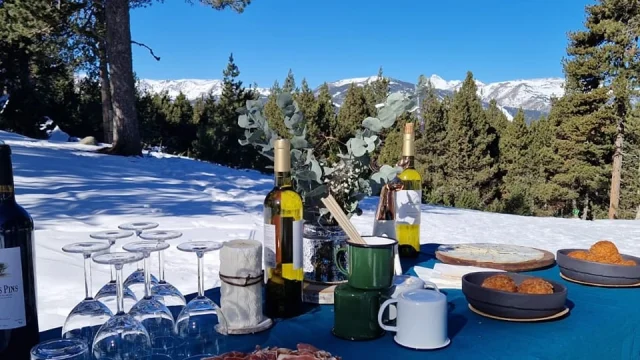 Table dressée pour un apéritif dans la neige avec vue sur les montagnes enneigées.