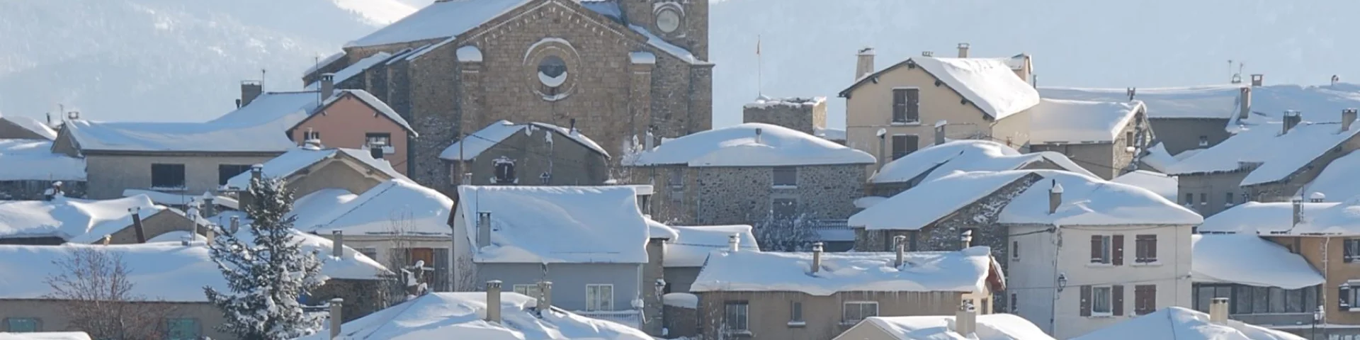 Vue sur le village de Font-Romeu couvert de neige, avec son église et les montagnes enneigées en arrière-plan.