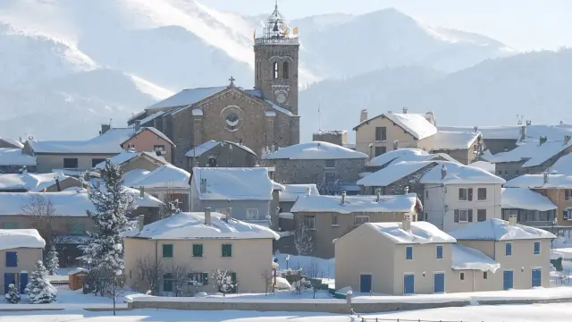 Vue sur le village de Font-Romeu couvert de neige, avec son église et les montagnes enneigées en arrière-plan.