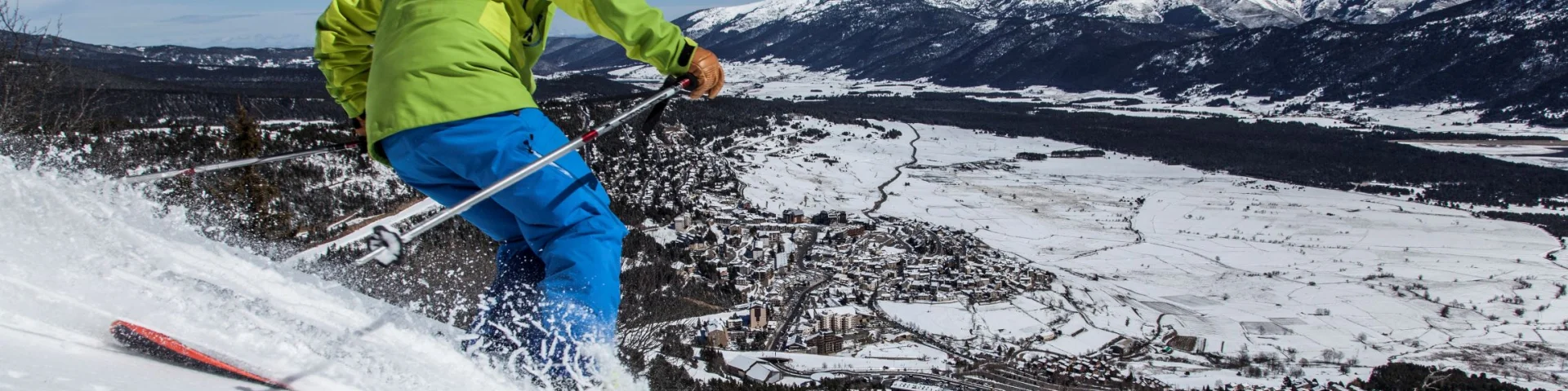 Skieur en descente sur une piste enneigée surplombant le village des Angles et la vallée recouverte de neige, sous un ciel bleu.