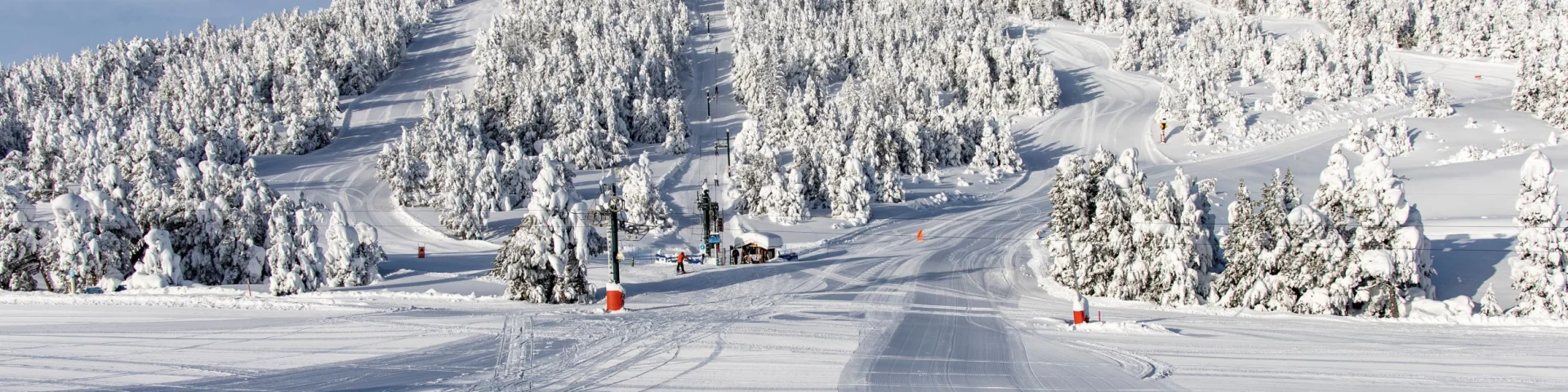 Vue sur les pistes enneigées de la station des Angles, bordées de forêts de sapins sous un ciel bleu dégagé.